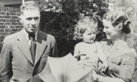 A black and white image of a man standing next to a woman holding a child and an umbrella.