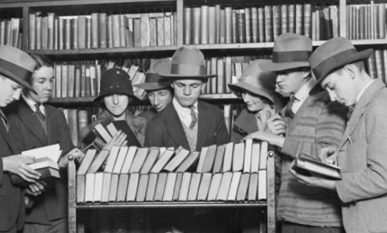 Nine people gathered around trolley of books in a library