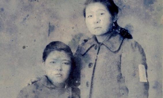 A black and white image of two women. One is seated and the other is standing with her arm around the seated woman.
