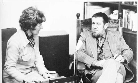 A woman sitting talking to a man while using a recorder.