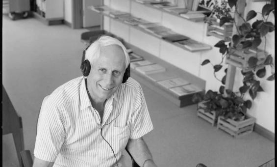 Black and white photo of a man listening to a recording with a pen in hand and a piece of paper next to him