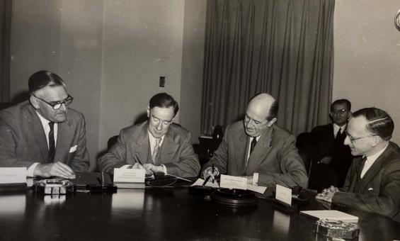 Four men seated at a table and one man sitting behind them