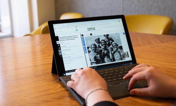 Over the shoulder of woman using laptop. On her screen she is using Trove to look at a digitised photo of nurses