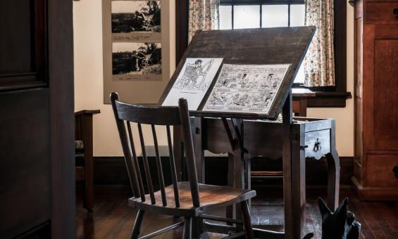 Easel, with two illustrated pages on it, and chair in May Gibbs' studio in Nutcote