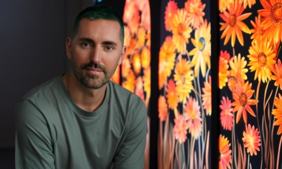 Matt Aberline sitting in front of an illuminated painting of wildflowers