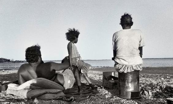 Black and white image of a man, woman and child sitting at a beach looking out towards the ocean