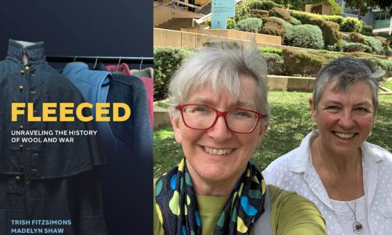 On the left is the cover of the book 'Fleeced: Unraveling the history of wool and war' by Trish Fitzsimons and Madelyn Shaw. On the right are two smiling women outside on a sunny day with grass and bushes in the background.