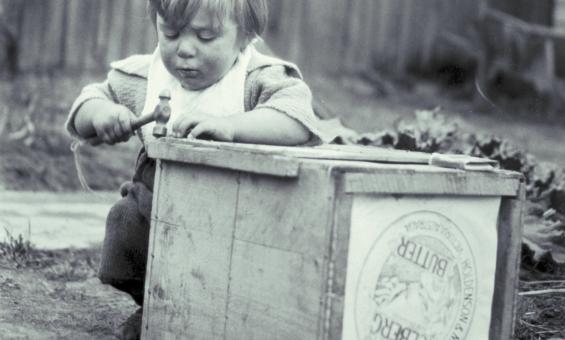 Black and white photo of a small child playing with a wooden box and a hammer