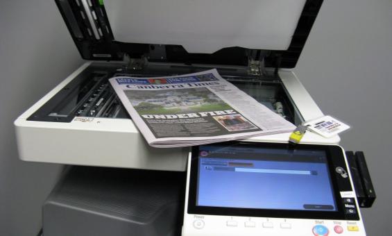 A multi-function device (print, photocopy, scan) with its top open and a newspaper placed on the glass 