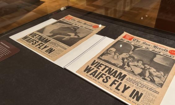 Two newspaper front covers in a display case. The headline on both reads, 'Vietnam waifs fly in'.