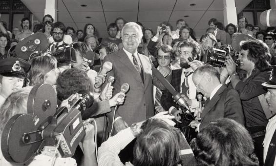 Black and white photo of Gough Whitlam speaking at Parliament House surrounded by reporters