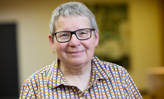 A short haired woman with black rimmed glasses in a checkered, button down shirt, smiling at the camera