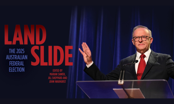A man in a suit and red tie stands at a lecturn in front of a blue curtain