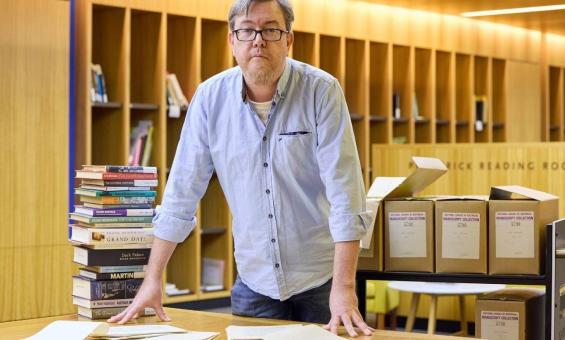 A man in a blue shirt leaning over a desk with papers and books